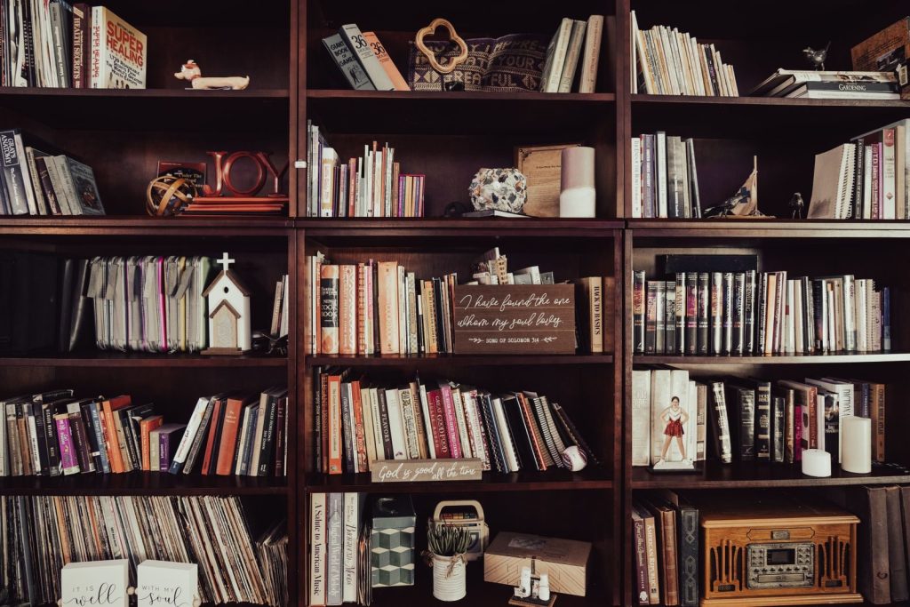 Warm-toned bookshelf filled with diverse books, religious decor, and trinkets.